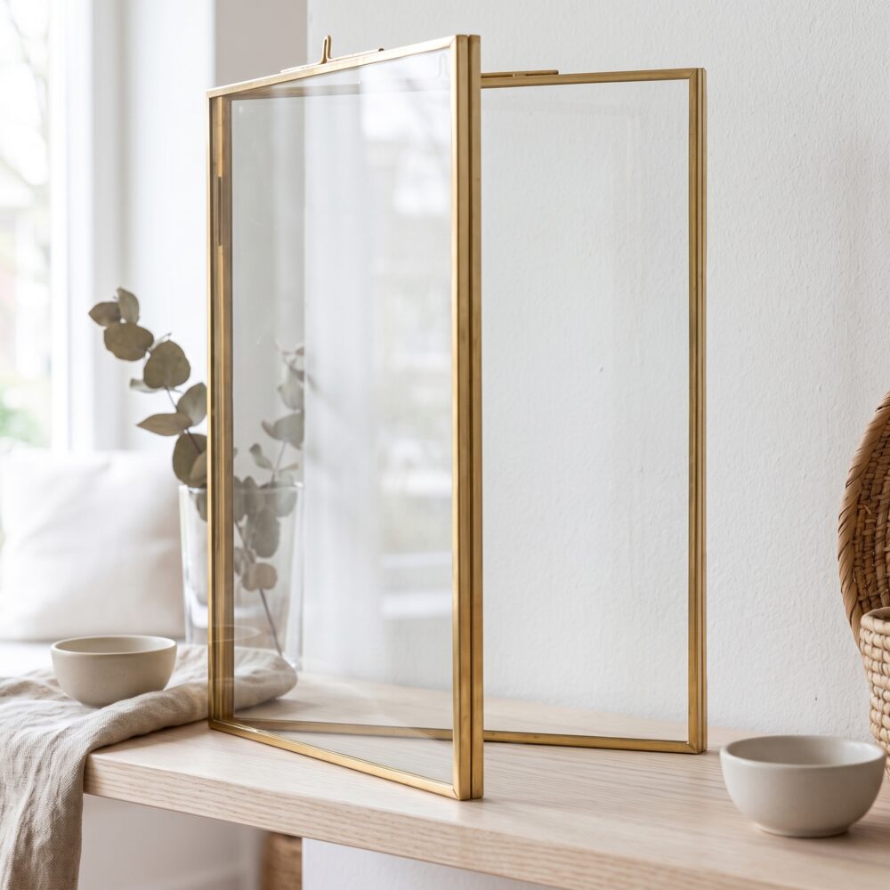 Gouden glazen fotolijst zonder foto op een lichte houten plank in een rustige woonkamer