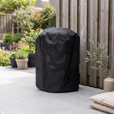 Zwarte barbecuehoes om een barbecue op een terras naast een houten schutting en tuinplanten