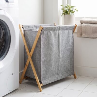 Grijze wasmand met houten frame naast een witte wasmachine in een lichte wasruimte