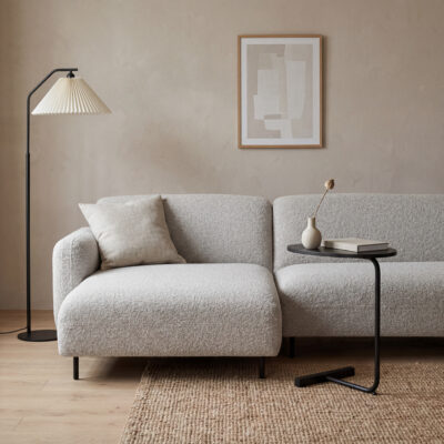 Lichte woonkamer met beige hoekbank, zwarte bijzettafel, vloerlamp en neutrale wanddecoratie