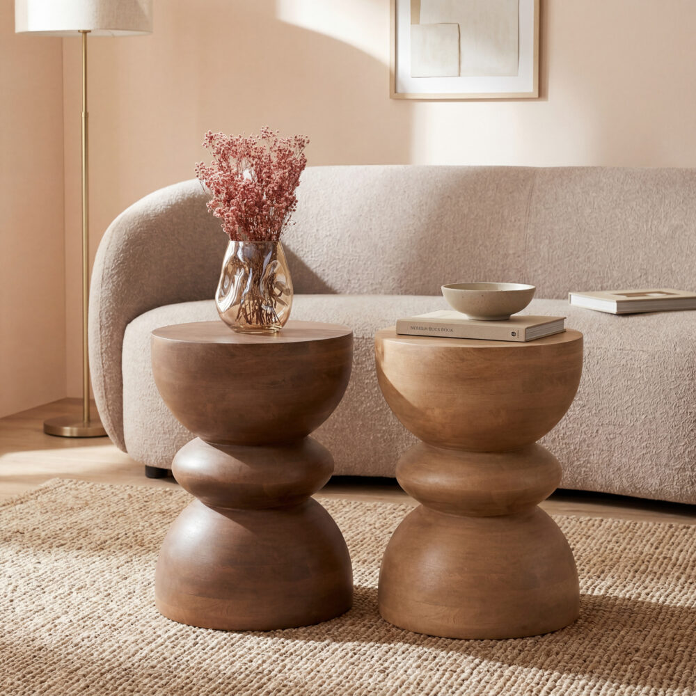 Warme woonkamer met twee sculpturale houten bijzettafels, beige bank, vaas met roze droogbloemen en vloerlamp