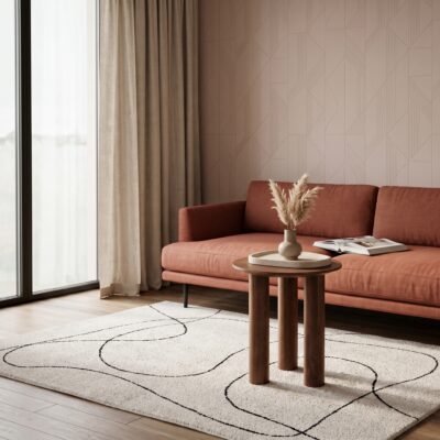 Warme woonkamer met terracottakleurige bank, ronde houten bijzettafel, licht vloerkleed met zwart lijnpatroon en droogbloemen