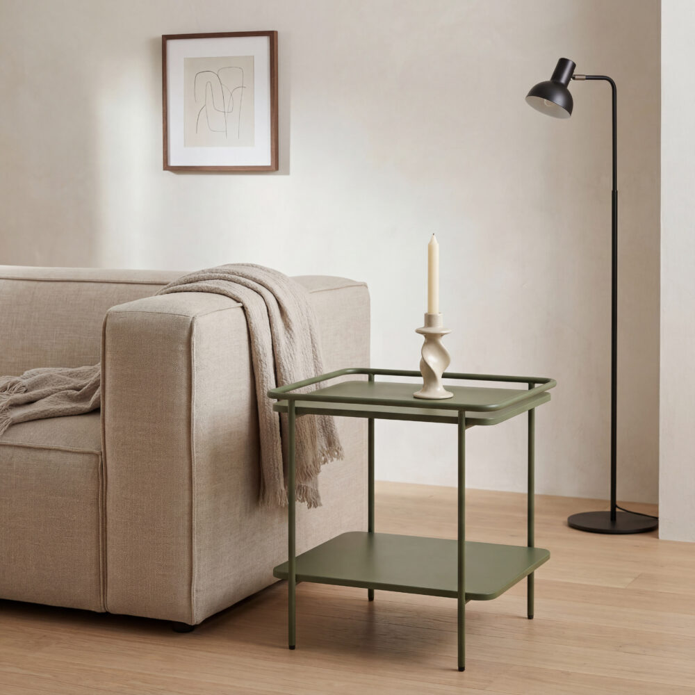 Groene metalen bijzettafel met twee niveaus en beige kandelaar naast een lichte bank met zwarte vloerlamp