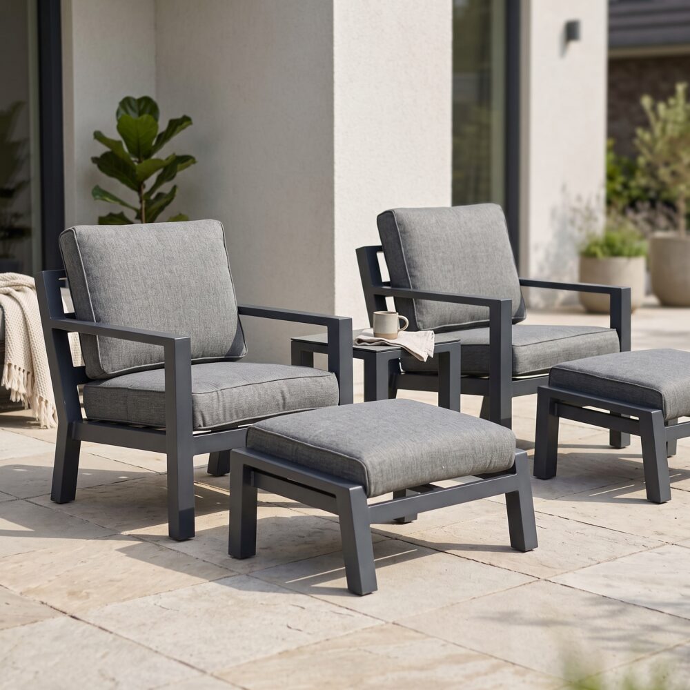 Grijze loungeset met twee fauteuils, voetenbankjes en bijzettafel op een zonnig terras