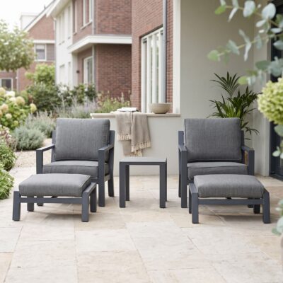 Grijze loungeset met twee fauteuils, voetenbankjes en bijzettafel op een licht terras met groene planten