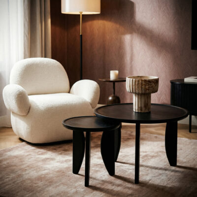 Warme woonkamer met witte loungestoel, twee zwarte ronde salontafels en vloerlamp.